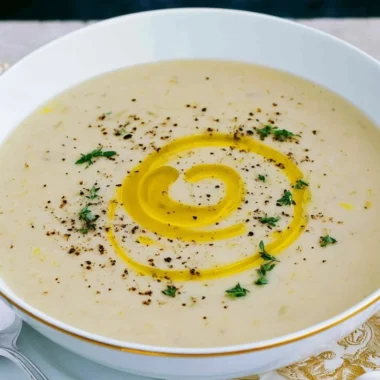 A bowl of creamy potato leek soup garnished with fresh herbs.