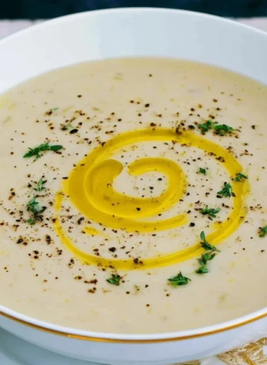 A bowl of creamy potato leek soup garnished with fresh herbs.