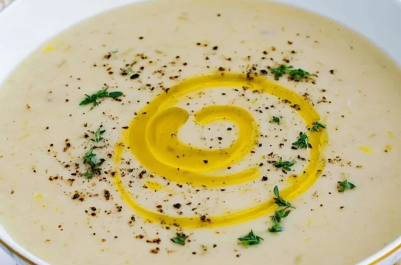 A bowl of creamy potato leek soup garnished with fresh herbs.
