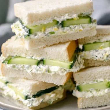 Delicious cucumber sandwich on white bread garnished with herbs.